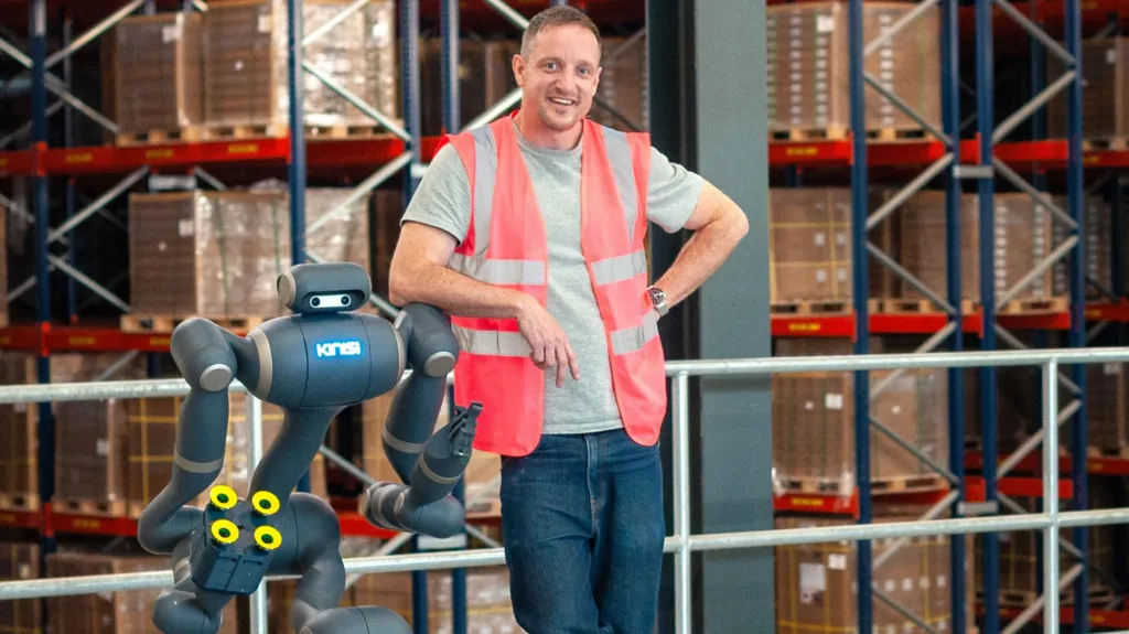 Bren Pierce leans against his robot in a warehouse