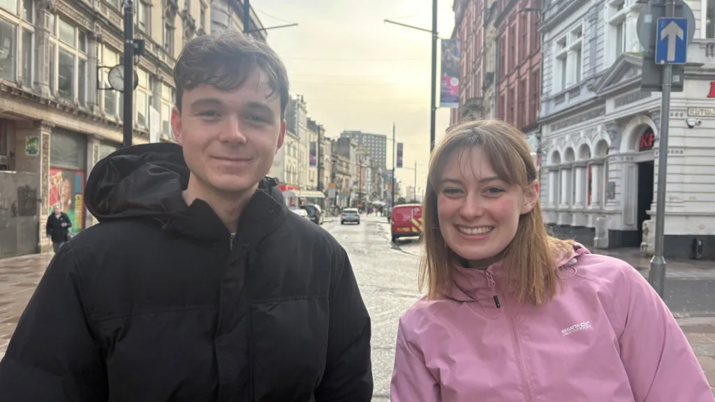 A man with brunette hair and a black puffer jacket smiling at the camera on the left, and a girl with light hair in a pink jacket smiling at the camera on the right