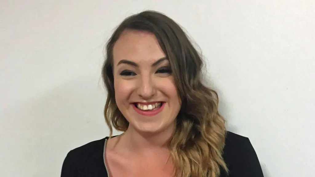 A young woman with curly brown hair smiles