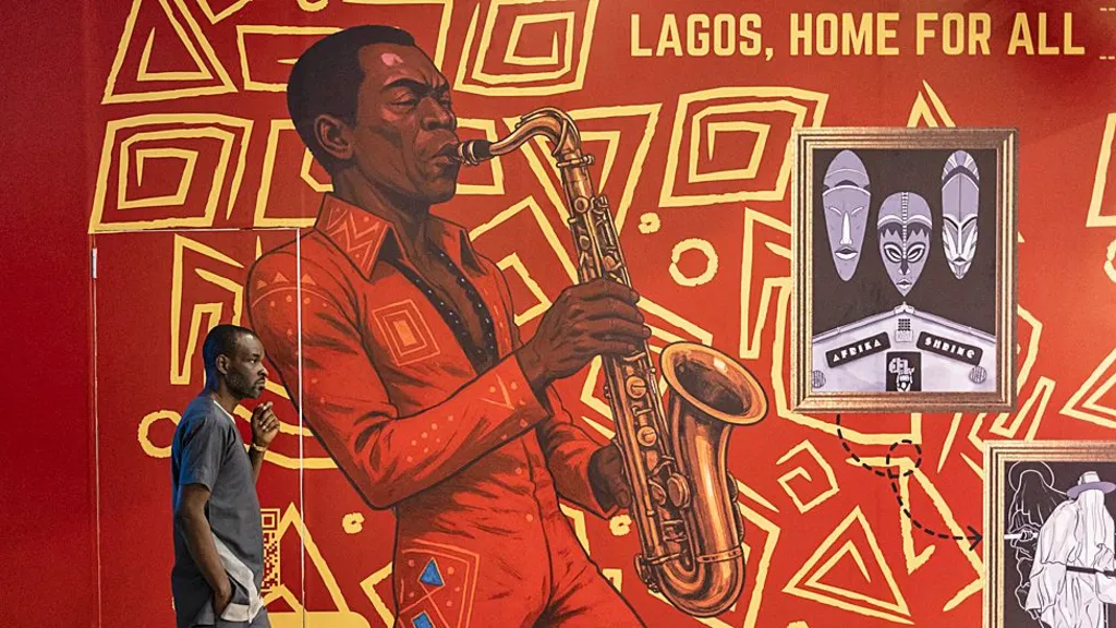 A man walks in front of mural in Lagos of Fela Kuti in a red jumpsuit playing a saxophone, with the words 'Lagos, Home For All'.